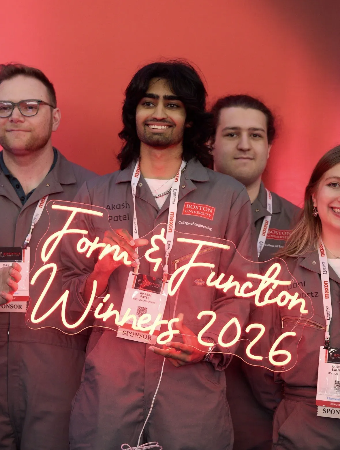 Akash Patel, center, holding the Form & Function Winners 2026 neon sign with BU Robotics Club teammates